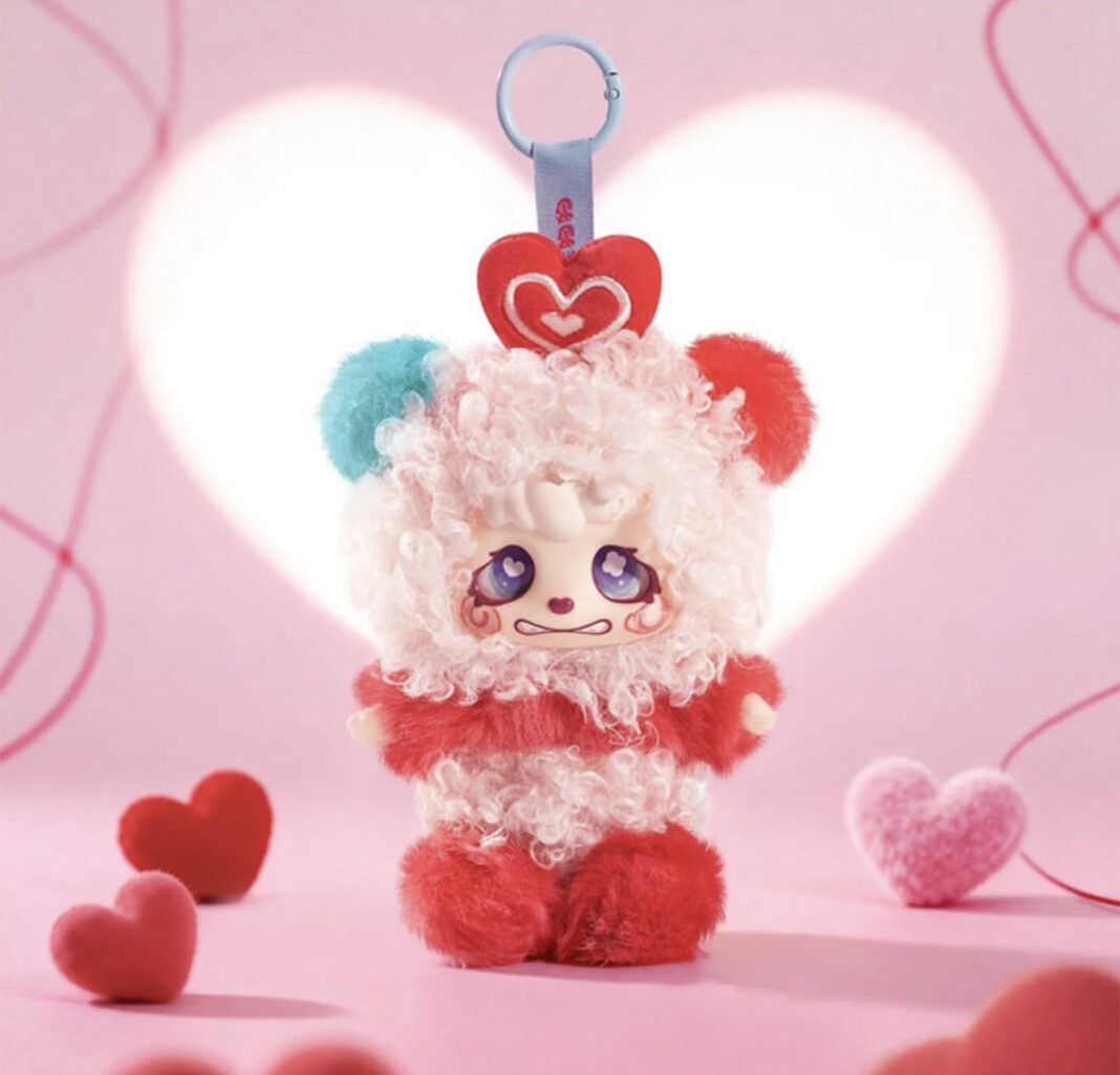 A close-up studio product photograph of a white and red Colliegogo Kacha Bear plush pendant toy, featuring a curly white fur head, a red body, mismatched ears, and a plush heart on its head against a glowing pink heart backdrop.