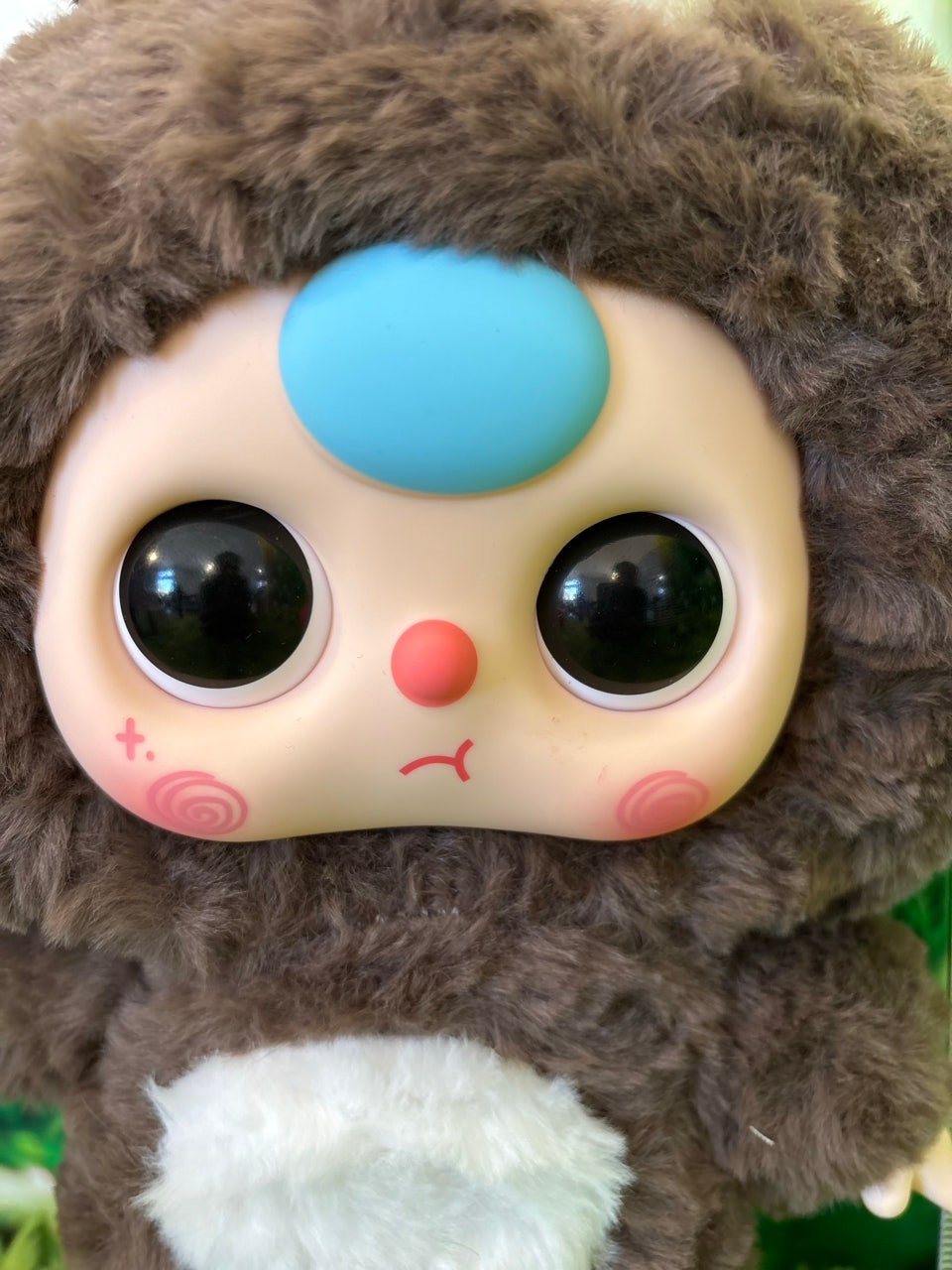 Extreme close up of the vinyl faceplate showing large black eyes, blue forehead charm, and pink swirly cheeks.