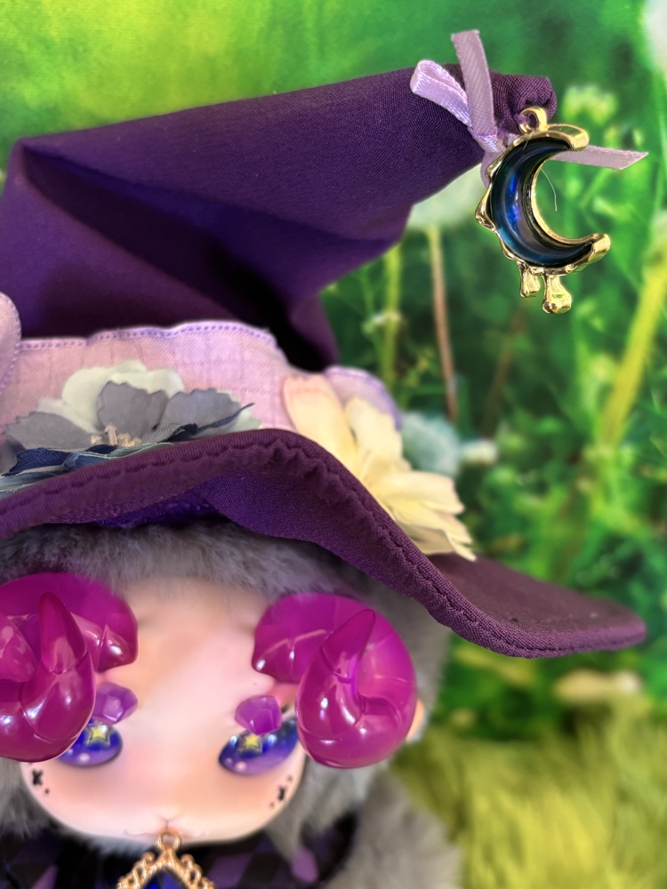 Detailed close up of a gold and dark blue crescent moon charm hanging from the tip of a purple witch hat.