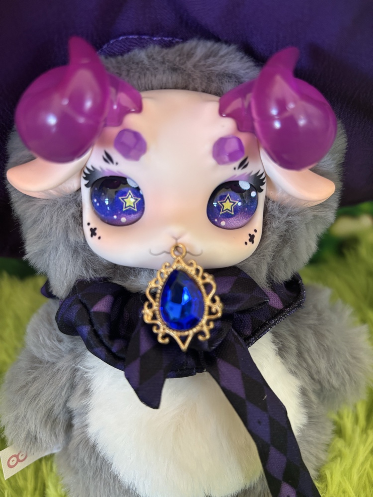 Close up of Fecoco Purple Galaxy plush showing translucent purple horns, star eyes, and a blue gem collar charm.
