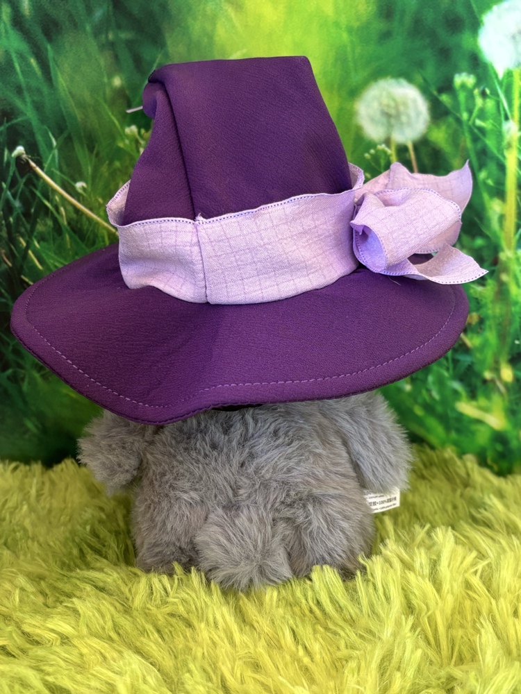 Back view of a gray fuzzy plush sheep wearing a purple witch hat with a wide lavender ribbon bow.