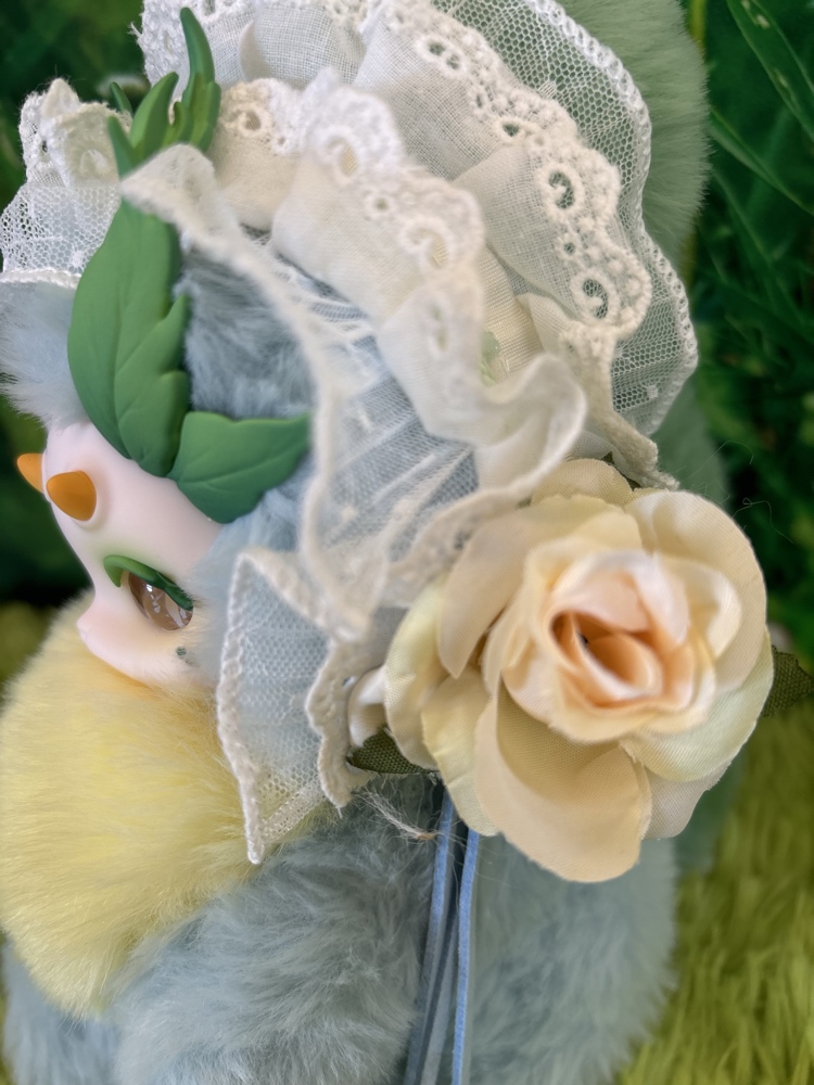 Close up side view of the Tutulong Herbalist plush focusing on a vintage cream-colored fabric rose and ruffled white lace.